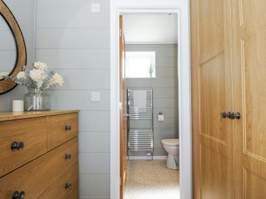 A hallway with wooden wardrobes and a chest of drawers leading to a bathroom with a toilet towel rail and a small window at 17 Meadow Retreat in Dobwalls