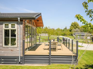 A wooden deck with a table and chairs outside a cabin with large windows at 17 Meadow Retreat in Dobwalls