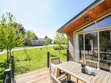 A wooden patio with a table and chairs next to a house with glass doors and a grassy yard with trees at 17 Meadow Retreat in Dobwalls