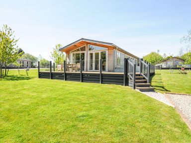 A wooden cabin with a deck and outdoor furniture on a grassy lawn at 17 Meadow Retreat in Dobwalls