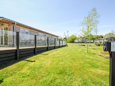 A grassy lawn with small trees next to wooden buildings with glass railings at 17 Meadow Retreat in Dobwalls
