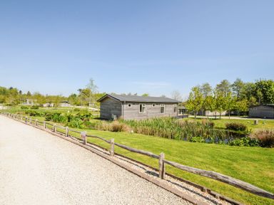 A wooden cabin near a pond with plants along a gravel pathway at 17 Meadow Retreat in Dobwalls