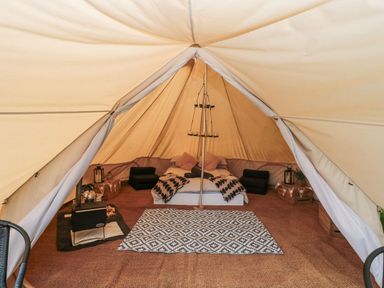 A bell tent interior with a bed cushions a stove and a patterned rug at Bell tent 4 in Camerton near Timsbury