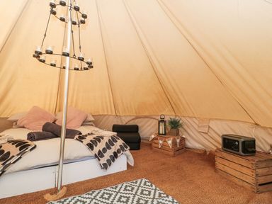 A tent interior with a bed blankets crates and a patterned rug at Bell tent 4 in Camerton near Timsbury