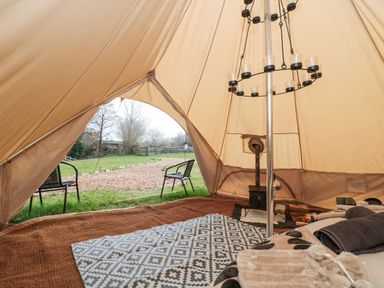 The interior of a bell tent with a bed, rugs, a wood stove, and two chairs outside at Bell tent 4 in Camerton near Timsbury
