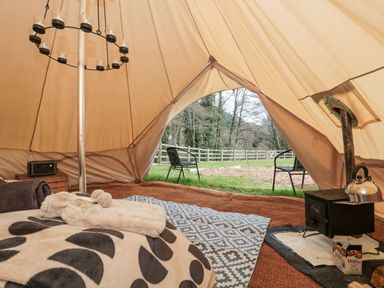 Inside a bell tent with a bed, stove with kettle, rug, chairs outside and view of trees and fence at Bell tent 4 in Camerton near Timsbury