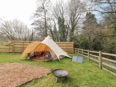 A garden with a bell tent, chairs, a fire pit, and wooden fencing at Bell tent 4 in Camerton near Timsbury