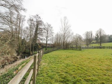 A grassy fenced field with trees and a small stream on the left at Bell tent 4 in Camerton near Timsbury