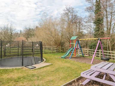 A backyard with a trampoline a colorful slide swing set and a wooden picnic table at Bell tent 4 Camerton near Timsbury