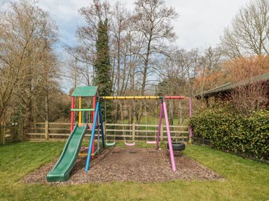A playground with a slide and swings in a grassy yard at Bell tent 4 in Camerton near Timsbury