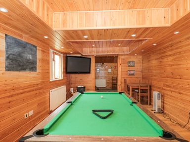A room with a pool table a wall-mounted television a small table with chairs and wooden panel walls at Bell tent 4 in Camerton near Timsbury