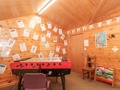 A wooden room with a foosball table a chair a wooden chair a book rack with books and papers on the wall at Bell tent 4 in Camerton near Timsbury