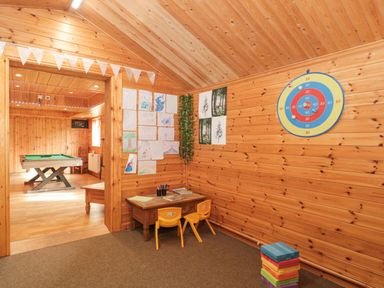 A wooden playroom with children's drawings on the wall a small table with two yellow chairs and a dartboard on the wall at Bell tent 4 Camerton near Timsbury
