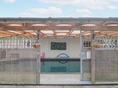An indoor swimming pool with a wooden pergola and lattice fencing at Bell tent 4 in Camerton near Timsbury