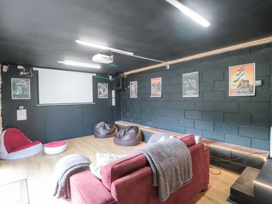 A home theater room with a projector screen red sofa bean bags and movie posters on black brick walls at Bell tent 4 Camerton near Timsbury