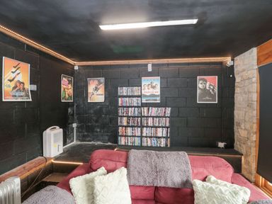 A room with black walls featuring movie posters a red sofa with cushions and throws and shelves with DVDs at Bell tent 4 Camerton near Timsbury