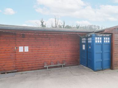 A wooden building with a blue police public call box and a metal bike rack in front at Bell tent 4 in Camerton near Timsbury