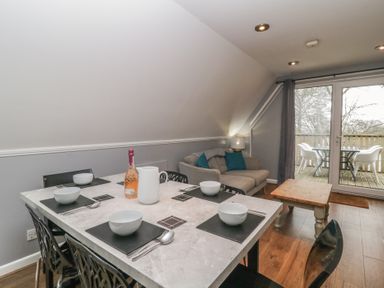 A dining area with a table set for four bowls and cutlery with a sofa and coffee table near sliding glass doors leading to a balcony at Valley Lodge 38 in St Ann's Chapel Cornwall