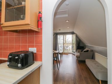 A kitchen countertop with a black toaster and a fire extinguisher mounted next to a doorway leading to a living room with a sofa dining table and glass doors opening to a balcony at Valley Lodge 38 in St Ann's Chapel Cornwall