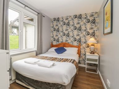 A bedroom with a double bed next to a window with grey curtains and a bedside table with a lamp at Valley Lodge 38 in St Ann's Chapel Cornwall