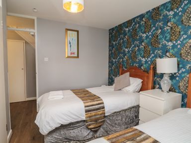 A bedroom with two single beds white bedside table lamp and peacock wallpaper at Valley Lodge 38 in St Ann's Chapel Cornwall