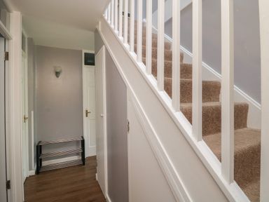 A hallway with carpeted stairs white railings and a small metal shoe rack at Valley Lodge 38 in St Ann's Chapel Cornwall