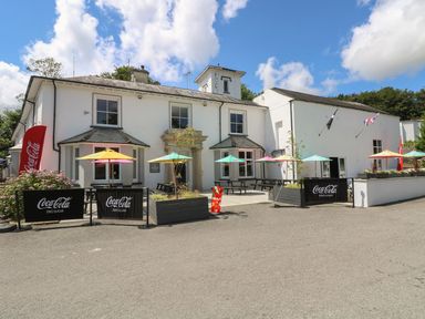 An outdoor seating area with tables and colorful umbrellas in front of a white building at Valley Lodge 38 in St Ann's Chapel Cornwall