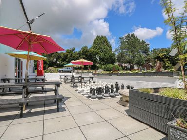 An outdoor patio with picnic tables and colorful umbrellas and a large chess set at Valley Lodge 38 in St Ann's Chapel Cornwall