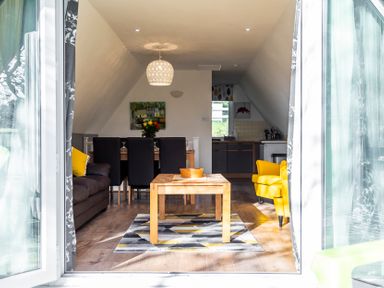 A living room with a wooden coffee table and yellow armchairs near a dining table and kitchen at Valley Lodge 40 in St Ann's Chapel Cornwall