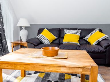 A living room with a wooden coffee table and black sofa with yellow and striped cushions at Valley Lodge 40 in St Ann's Chapel Cornwall