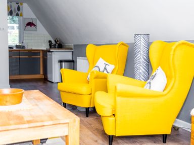 Two yellow armchairs with bicycle print cushions in a living area next to a wooden coffee table and kitchen in Valley Lodge 40 St Ann's Chapel Cornwall