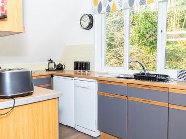 A kitchen with a toaster kettle tea set clock and window at Valley Lodge 40 in St Ann's Chapel Cornwall