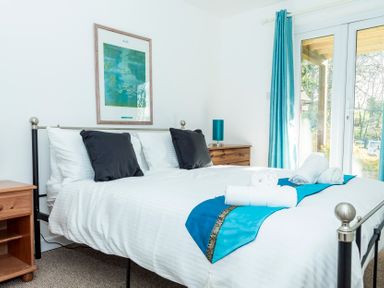 A bedroom with a double bed with white sheets and black pillows and a blue runner at Valley Lodge 40 in St Anns Chapel Cornwall