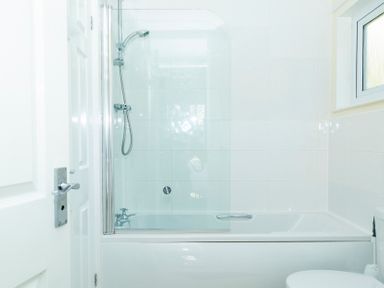 A bathroom with a bathtub shower combination with glass screen a window and a toilet at Valley Lodge 40 St Ann's Chapel Cornwall