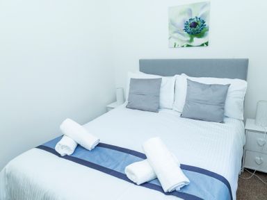 A bedroom with a bed made with white linens and blue runner with towels and gray pillows and bedside tables with lamps at Valley Lodge 40 in St Ann's Chapel Cornwall