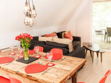 A dining table set with red heart-shaped placemats and a vase of flowers next to a living area with a dark sofa and cushions at Valley Lodge 3 St Ann's Chapel Cornwall
