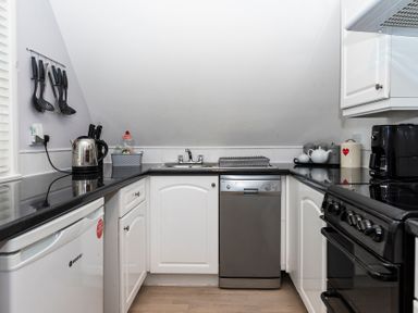 A kitchen with black countertops white cabinets a dishwasher stove kettle and kitchen utensils at Valley Lodge 3 St Ann's Chapel Cornwall