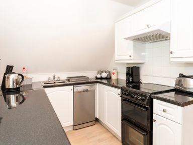 A kitchen with black countertops white cabinets a dishwasher a black stove a coffee maker a kettle and a toaster at Valley Lodge 3 in St Ann's Chapel Cornwall