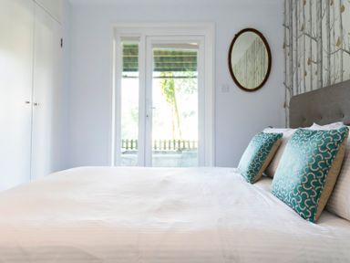 A bedroom with a bed with two patterned pillows a round mirror on the wall and a glass door at Valley Lodge 3 in St Ann's Chapel Cornwall