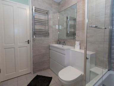 A bathroom with a sink, toilet, towel rack, mirror, and bathtub with shower at Valley Lodge 3 in St Ann's Chapel Cornwall