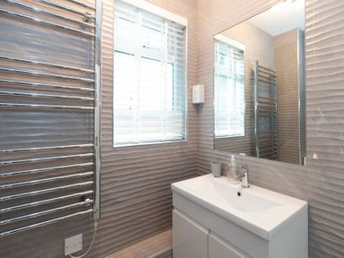 A bathroom with a sink cabinet mirror and a heated towel rail next to a window with blinds at Valley Lodge 3 St Ann's Chapel Cornwall