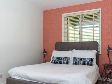 A bedroom with a bed with white bedding two blue patterned pillows two small side tables with lamps and a window with blinds at Valley Lodge 3 in St Ann's Chapel Cornwall