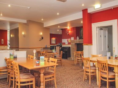 A dining room with multiple wooden tables and chairs and red and beige walls at Valley Lodge 3 St Anns Chapel Cornwall