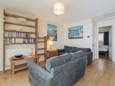A living room with gray sofas wooden shelves and a wooden table at 26 Manorcombe in St Ann's Chapel Cornwall