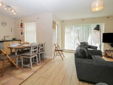 A combined kitchen and living room with a dining table set and chairs a sofa armchair and large windows with vertical blinds at 26 Manorcombe St Ann's Chapel Cornwall