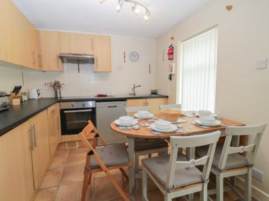 A kitchen with wooden cabinets a dining table set with dishes and four chairs at 26 Manorcombe in St Ann's Chapel Cornwall