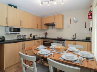 A kitchen with wooden cabinets a dining table set for six with bowls plates and utensils at 26 Manorcombe in St Ann's Chapel Cornwall
