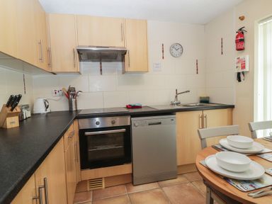 A kitchen with wooden cabinets black countertop oven dishwasher sink and a dining table with plates at 26 Manorcombe St Ann's Chapel Cornwall