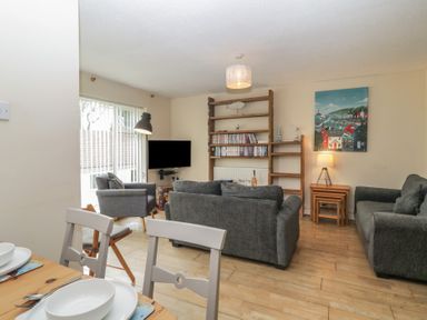 A living room with grey sofas a wooden dining table and chairs a wooden bookshelf and a TV at 26 Manorcombe in St Ann's Chapel Cornwall