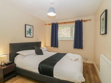 A bedroom with a double bed nightstand and window with blue curtains at 26 Manorcombe in St Ann's Chapel Cornwall
